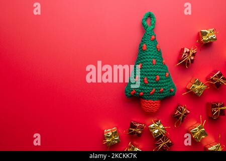 Gestrickter Weihnachtsbaum mit vielen Geschenken auf rotem Hintergrund Stockfoto
