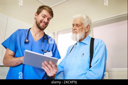 Lassen Sie mich Sie durch meinen Behandlungsplan führen. Ein junger Arzt erklärt seinem älteren Patienten mit einer Tablette eine Diagnose. Stockfoto