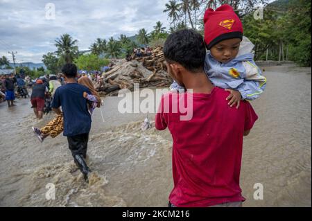 Nach einer weiteren Sturzflut im Dorf Rogo, Bezirk South Dolo, Sigi Regency, Provinz Zentral-Sulawesi, Indonesien, überqueren die Bewohner am 6. September 2021 eine mit Wasser und Schlamm bedeckte Straße mit Kindern. Nachdem das Dorf am Samstag (29. August 2021) von Sturzfluten heimgesucht wurde, wurde es am Sonntag (5. September 2021) in der Nacht erneut von einer Sturzflut heimgesucht, die dazu führte, dass Dutzende von Häusern in Schlamm getaucht wurden und Hunderte von Bewohnern an sichere Orte zurückkehrten. Die Sturzflut im Dorf war das vierte Mal seit November 2020. Die Topographie des Gebietes am Fuße eines Stockfoto