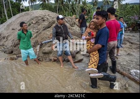 Nach einer weiteren Sturzflut im Dorf Rogo, Bezirk South Dolo, Sigi Regency, Provinz Zentral-Sulawesi, Indonesien, überqueren die Bewohner am 6. September 2021 eine mit Wasser und Schlamm bedeckte Straße mit Kindern. Nachdem das Dorf am Samstag (29. August 2021) von Sturzfluten heimgesucht wurde, wurde es am Sonntag (5. September 2021) in der Nacht erneut von einer Sturzflut heimgesucht, die dazu führte, dass Dutzende von Häusern in Schlamm getaucht wurden und Hunderte von Bewohnern an sichere Orte zurückkehrten. Die Sturzflut im Dorf war das vierte Mal seit November 2020. Die Topographie des Gebietes am Fuße eines Stockfoto