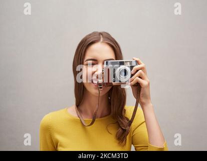 Sagen Sie Käse. Studioportrait einer attraktiven jungen Fotografin, die mit ihrer Kamera vor grauem Hintergrund posiert. Stockfoto