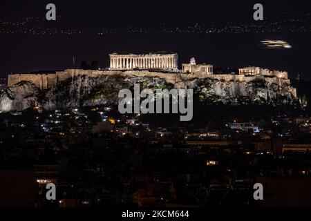 Nachtansicht des Parthenon und der Akropolis mit einer Fähre, die im Hintergrund in der griechischen Hauptstadt Athina vorbeifährt. Langzeitbelichtung Fotografie Technik zeigt die Antiquitäten im Dunkeln beleuchtet mit der städtischen Landschaft der Stadt um.. Der alte Hügel der Akropolis, einschließlich des weltweit bekannten marmorierten Tempels Parthenon und der Überreste vieler antiker Gebäude von großer architektonischer und historischer Bedeutung wie dem Erechtheion, Propylaia, dem Tempel der Athene Nike, den Karyaden und mehr. Während der osmanischen Besatzung wurde die Akropolis schwer beschädigt. Es ist heute UNESCO-Welterbe Stockfoto