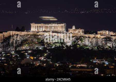 Nachtansicht des Parthenon und der Akropolis mit einer Fähre, die im Hintergrund in der griechischen Hauptstadt Athina vorbeifährt. Langzeitbelichtung Fotografie Technik zeigt die Antiquitäten im Dunkeln beleuchtet mit der städtischen Landschaft der Stadt um.. Der alte Hügel der Akropolis, einschließlich des weltweit bekannten marmorierten Tempels Parthenon und der Überreste vieler antiker Gebäude von großer architektonischer und historischer Bedeutung wie dem Erechtheion, Propylaia, dem Tempel der Athene Nike, den Karyaden und mehr. Während der osmanischen Besatzung wurde die Akropolis schwer beschädigt. Es ist heute UNESCO-Welterbe Stockfoto