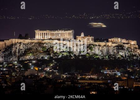 Nachtansicht des Parthenon und der Akropolis mit einer Fähre, die im Hintergrund in der griechischen Hauptstadt Athina vorbeifährt. Langzeitbelichtung Fotografie Technik zeigt die Antiquitäten im Dunkeln beleuchtet mit der städtischen Landschaft der Stadt um.. Der alte Hügel der Akropolis, einschließlich des weltweit bekannten marmorierten Tempels Parthenon und der Überreste vieler antiker Gebäude von großer architektonischer und historischer Bedeutung wie dem Erechtheion, Propylaia, dem Tempel der Athene Nike, den Karyaden und mehr. Während der osmanischen Besatzung wurde die Akropolis schwer beschädigt. Es ist heute UNESCO-Welterbe Stockfoto