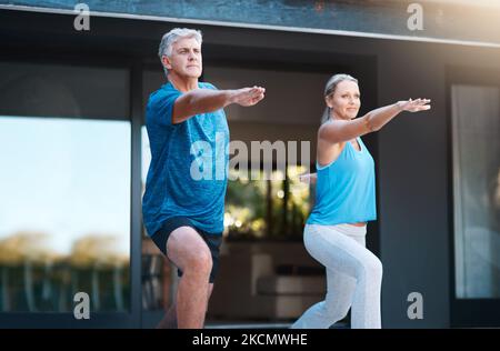 Ein reifes und glückliches Paar, das Yoga-Übungen außerhalb ihres Hauses macht. Stockfoto
