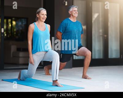 Gleichgewicht ist der Schlüssel zu jedem Vermögen des Lebens. In voller Länge ein reifes und glückliches Paar, das außerhalb ihres Hauses Yoga-Übungen macht. Stockfoto