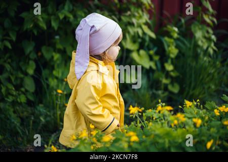 Nettes Mädchen in einer gelben Jacke sammelt Blumen auf einer Wiese. Ein Kind stand im frischen grünen Gras zwischen den Frühlingsblumen. Ein kleines Kind macht eine Bouq Stockfoto