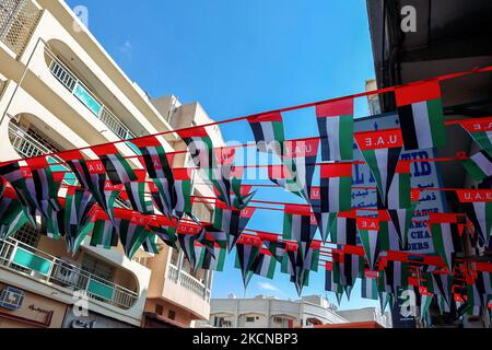 VAE, Dubai - 29. November 2021: Hängende Dekorationen von vielen Nationalflaggen der Vereinigten Arabischen Emirate auf der Straße von Dubai. Natoinal Day VAE. Fahnen in Reihen winken im Wind gegen den blauen Himmel. Stockfoto