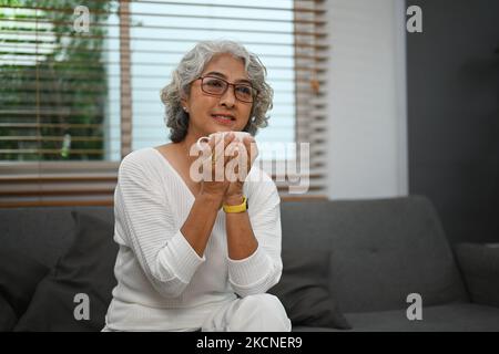 Glückliche Frau mittleren Alters, die sich auf der Couch entspannt und ihren Morgenkaffee genießt Stockfoto