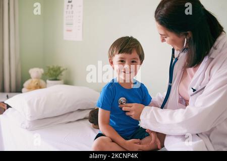 Der Arzt sagt, ich bin jetzt ein großer Junge. Eine Ärztin überprüft die Herzfrequenz ihrer jungen Patienten. Stockfoto