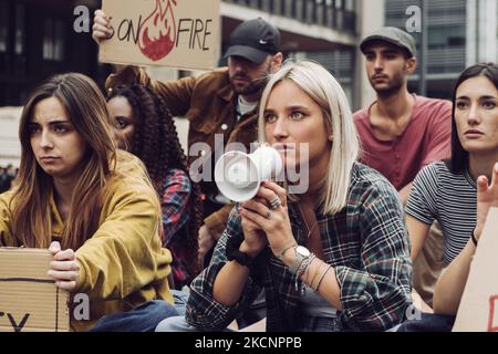 Junge Protestierende Sit-in - Gruppe von Generation z Menschen protestieren gegen die globale Erwärmung mit Megaphon und Plakaten - Menschen Lifestyle-Konzept Stockfoto