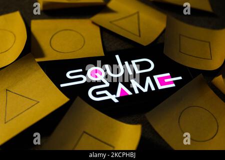 Das Logo der Squid Game-Serie, das auf einem Telefonbildschirm angezeigt wird, und die aus der Serie bekannten Symbole, die auf Papierstücken gezeichnet sind, sind auf diesem Illustrationsfoto zu sehen, das am 13. Oktober 2021 in Krakau, Polen, aufgenommen wurde. (Foto von Jakub Porzycki/NurPhoto) Stockfoto