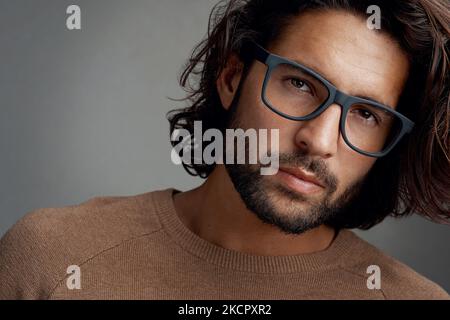 Auffällige Rahmen, die zu seinem Gesicht passen. Studioaufnahme eines hübschen jungen Mannes, der eine Brille vor grauem Hintergrund trägt. Stockfoto