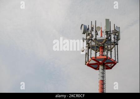 5G Telekommunikationsturm- und Mikrowellenantennen auf einem rot-weißen Mast, der gegen den bewölkten Himmel mit verschiedenen Antennentypen und Geschirr aufgestellt ist Stockfoto