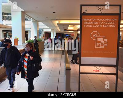 Menschen laufen an einem Schild vorbei, auf dem sie darüber informiert werden, dass während der neuartigen Coronavirus-Pandemie (COVID-19) am 23. Oktober 2021 in Toronto, Ontario, Kanada, Impfnachweise erforderlich sind, um in einem Lebensmittelgericht eines Einkaufszentrums zu speisen. Alle Einwohner von Ontario, die 12 Jahre und älter sind, müssen einen Impfnachweis vorlegen, um in Restaurants zu Abend zu essen sowie Fitnessstudios, Kinos und andere risikoreiche Innenräume zu besuchen. Die Provinz Ontario kündigte einen Plan an, bis März alle verbleibenden Einschränkungen der öffentlichen Gesundheit aufzuheben, einschließlich der obligatorischen Maskenbestellung und des Impfpass-Systems, das nur wirksam wurde Stockfoto