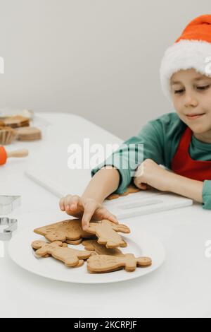 Ein süßer Junge in einem Weihnachtsmütze greift nach einem frisch gebackenen Weihnachtsgebäck. Weihnachtsferien. Stockfoto