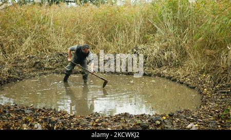 Pfütze Sumpf graben Hacke Arbeiter Mann Pfütze Schutz Erhaltung Natur aus Bau einer Amphibienzucht neuen Baggerteich von Hand. Sumpfflosse in Feuchtgebieten Stockfoto