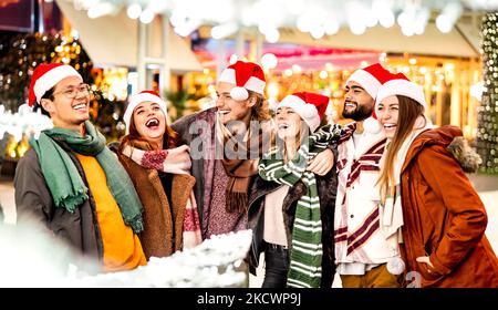 Fröhliche Freunde Gruppe zu Fuß in der Stadt in den Weihnachtsferien - Winter Lifestyle-Konzept mit multikulturellen jungen Menschen tragen roten santa Hüte mit Fu Stockfoto