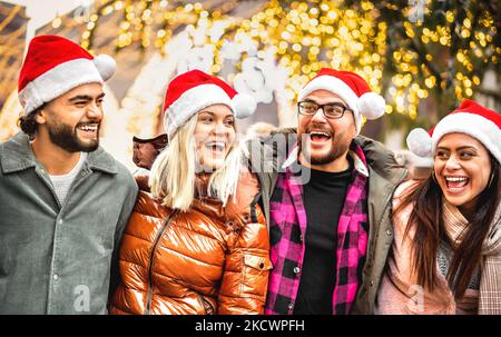 Happy friends Gruppe zu Fuß in der Stadt unter Weihnachtsbaum Dekorationen - Winter Lifestyle-Konzept mit jungen Menschen tragen roten weihnachtsmann Hüte haben Stockfoto