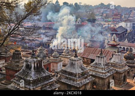 Rauch von einem Körper, der eingeäschert wird, der unter den vielen Chaityas und anderen Gebäuden im Hindu-Tempelkomplex in Pashupatinath, Nepal, zu sehen ist. Im Hintergrund steigt Rauch aus den Kremierungsghats auf, während ein Leichnam am Ufer des Flusses Bagmati eingeäschert wird. Der Komplex in Pashupatinath ist der heiligste Hindu-Ort in Nepal. (Foto von Creative Touch Imaging Ltd./NurPhoto) Stockfoto