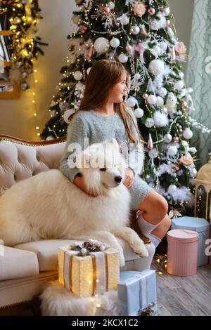 Kleines niedliches Mädchen, das mit einem Samoyed-Hund auf dem Sofa sitzt Stockfoto