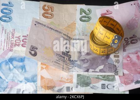 Foto Illustration von türkischen Lira-Banknoten auf schwarzem Hintergrund und einem Maßband als Symbol für die schrumpfende Wirtschaft und Währung. Die Lira erreicht ein neues Rekordtief, da die Währung die Verluste für den Handel über 13,73 pro US-Dollar und 15,51 Euro ausdehnte. Die türkische Lira rutscht auf ein Rekordtief, nachdem Präsident Erdogan die Leitzinspolitik verdoppelt hat. Illustration der türkischen Lira-Banknoten, die Währung der Türkei, in türkischer Sprache Türk Lira genannt, mit dem Zeichen: Und Code TRY oder TL. Auf der Vorderseite des Gesetzentwurfs sind Porträts von Mustafa Kemal Atatürk zu sehen. Amsterdam, Niederlande am 33. Dezember 2021. (Foto von Nicol Stockfoto