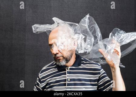 Reifer Mann mit einer transparenten Plastiktüte, die über Kopf und Gesicht fliegt. Ersticken. Gesicht in einer Plastiktüte, Strangulation Stockfoto