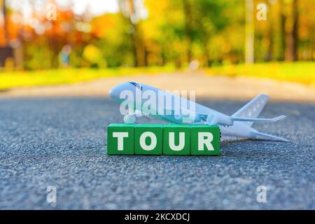 WORTTOUR aus hölzernen Alphabet-Blöcken, die vor einem Spielzeug-Flugzeug im Freien platziert wurden. Stockfoto