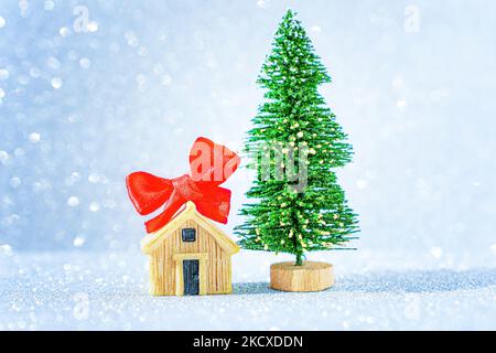 Miniatur-Hausmodell mit roter Schleife von einem Spielzeug Weihnachtsbaum vor einem funkelnden Hintergrund verziert. Stockfoto