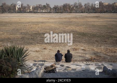 Zwei iranische Männer sitzen am 14. Dezember 2021 in Isfahan, 450 km (281 Meilen) südlich von Teheran, am ausgetrockneten Fluss Zayandeh Rud. Zayandeh Rud ist eine der Haupttouristenattraktionen von Isfahan, die vollständig ausgetrocknet ist, auch historische Brücken auf dem Fluss können durch das Absinken des Zayandeh Rud Flussbett beschädigt werden, wenn die Dürre anhält. (Foto von Morteza Nikoubazl/NurPhoto) Stockfoto