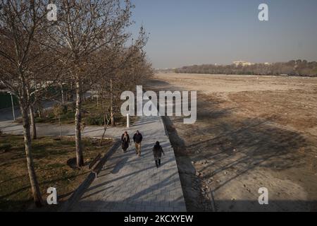 Die Iraner gehen am 14. Dezember 2021 an einem ausgetrockneten Fluss des Zayandeh Rud in der Stadt Isfahan, 450 km (281 Meilen) südlich von Teheran entlang. Zayandeh Rud ist eine der Haupttouristenattraktionen von Isfahan, die vollständig ausgetrocknet ist, auch historische Brücken auf dem Fluss können durch das Absinken des Zayandeh Rud Flussbett beschädigt werden, wenn die Dürre anhält. (Foto von Morteza Nikoubazl/NurPhoto) Stockfoto