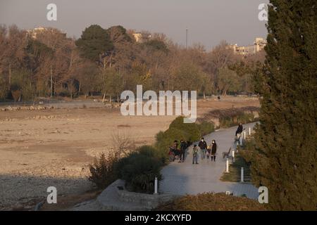 Die Iraner gehen am 14. Dezember 2021 an einem ausgetrockneten Fluss des Zayandeh Rud in der Stadt Isfahan, 450 km (281 Meilen) südlich von Teheran entlang. Zayandeh Rud ist eine der Haupttouristenattraktionen von Isfahan, die vollständig ausgetrocknet ist, auch historische Brücken auf dem Fluss können durch das Absinken des Zayandeh Rud Flussbett beschädigt werden, wenn die Dürre anhält. (Foto von Morteza Nikoubazl/NurPhoto) Stockfoto