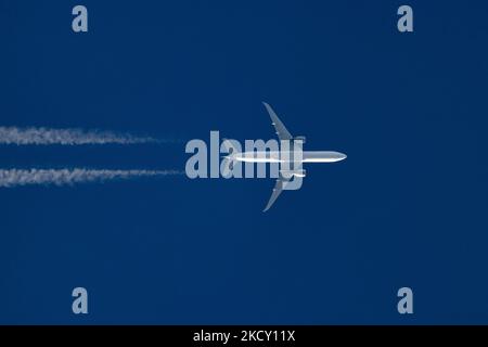 Ein weißes Flugzeug, das an einem sonnigen Tag über Europa in einer Höhe von 40,000 Metern am blauen Himmel fliegt, ein Flug an einem klaren Wintertag. Die Symboldarstellung des überfliegenden Großkörper-Düsenflugzeugs ohne Logo-Aufdruck auf dem Bauchboden des Rumpfes hinterlässt Kondensstreifen oder Kondensstreifen, eine weiße Dampflinie. Die Luft- und Passagierindustrie befindet sich in einer schwierigen Phase, da die Coronavirus-Pandemie Covid-19 negative Auswirkungen auf die Reisebranche hat und aufgrund der neuen Omega-Variantenmutation Angst vor einer Verschlechterung der Situation hat. Eindhoven, Niederlande auf D Stockfoto