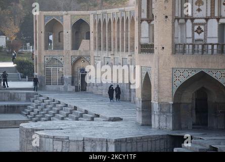 Zwei iranische Frauen mit Schutzmasken gehen am 14. Dezember 2021 nach dem Ausbruch des neuen Coronavirus (COVID-281 19) auf dem ausgetrockneten Fluss Zayandeh Rud in der Stadt Isfahan, 450 km südlich von Teheran, entlang der historischen Brücke von Khaju. Ein Sprecher der Isfahan University of Medical Sciences sagte: „Gemäß der jüngsten epidemischen Färbung der Covid-19-Krankheit befand sich die Metropole Isfahan in einem blauen (risikoarmen) Zustand, was proportional zur Abnahme der Anzahl positiver Koronartests und hospitalisierter Menschen ist.“ Laut einer Nachricht der iranischen Studenten News Age Stockfoto