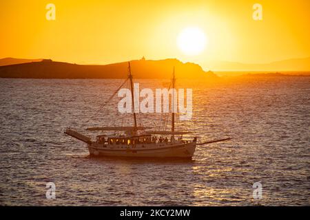 Ein Schiff, das vor der untergehenden Sonne vorbeifährt. Touristen genießen einen wunderschönen Sonnenuntergang während der magischen Stunde auf der Insel Mykonos in Griechenland. Die griechische Insel Myconos ist ein beliebtes glamouröses mediterranes Reiseziel für einen Urlaub in den Kykladen, der Ägäis mit den ikonischen weiß getünchten Gebäuden, den Sandstränden und berühmten Partys an den Strandbars. Die Tourismus- und Reisebranche hatte aufgrund der Coronavirus-Pandemie Covid-19 negative Auswirkungen auf die Wirtschaft und die lokale Wirtschaft. Mykonos, Griechenland am 10. Oktober 2021 (Foto von Nicolas Economou/NurPhoto) Stockfoto