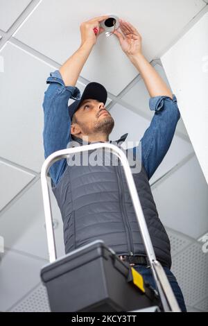 Mann steht auf Leiter wechseln eine Glühbirne Stockfoto