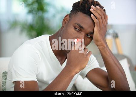 Junger Mann mit Gewebe in seinem Nasenloch hat Nasenbluten Stockfoto