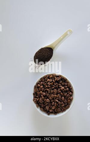 Weiße Schüssel mit Kaffeebohnen und Löffel gemahlenem Kaffee auf weißem Hintergrund. Stockfoto