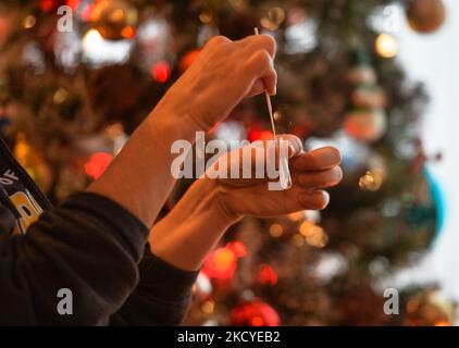 Eine Frau führt vor dem Weihnachtsbaum einen schnellen COVID-19-Antigentest durch, bevor sie sich ihrer Familie zum Weihnachtsessen anschließt. Das Rapid Response COVID-19 Antigen Rapid Test Device detektiert das Vorhandensein von SARS-CoV-2 viralen Nucleoprotein-Antigenen in nasalen und nasopharyngealen Sekreten. In nur 15 Minuten können Einzelpersonen ein positives oder negatives Ergebnis bestimmen. Am Freitag, den 24. Dezember 2021, Kanada. (Foto von Artur Widak/NurPhoto) Stockfoto