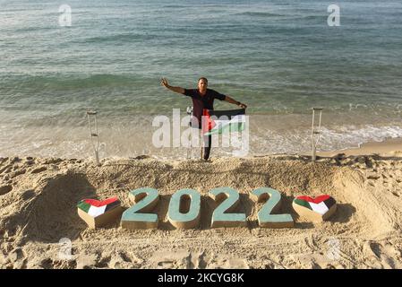 Ein Palästinenser Mohammed Totah ''32'', der am Strand von Gaza eine Sandzeichnung von 2022 anstellt und seine Hoffnung zum Ausdruck bringt, dass das neue Jahr das Friedensjahr Palästinas sein wird, am 28. Dezember 2021. Mohammed wurde nach israelischen Angriffen während des Gaza-Krieges am 28. Dezember 2008 im Führungskrieg gegen den Gazastreifen verletzt, der sein rechtes Bein verlor. Mohammed spricht über seine verheerende Verletzung, die sein Leben veränderte, ihn aber nicht von seinem Traum und seinem Streben nach einem guten Leben mit seiner Familie abgehalten hat. (Foto von Sameh Rahmi/NurPhoto) Stockfoto