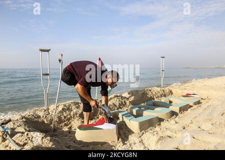 Ein Palästinenser Mohammed Totah ''32'', der am Strand von Gaza eine Sandzeichnung von 2022 anstellt und seine Hoffnung zum Ausdruck bringt, dass das neue Jahr das Friedensjahr Palästinas sein wird, am 28. Dezember 2021. Mohammed wurde nach israelischen Angriffen während des Gaza-Krieges am 28. Dezember 2008 im Führungskrieg gegen den Gazastreifen verletzt, der sein rechtes Bein verlor. Mohammed spricht über seine verheerende Verletzung, die sein Leben veränderte, ihn aber nicht von seinem Traum und seinem Streben nach einem guten Leben mit seiner Familie abgehalten hat. (Foto von Sameh Rahmi/NurPhoto) Stockfoto