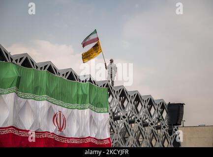 Ein Mitglied des Korps der Islamischen Revolutionsgarde (IRGC) schwenkt eine iranische Flagge und eine Flagge mit einem Porträt des iranischen Obersten Führers Ayatollah Ali Khamenei, während er auf einer Kundgebung auf dem Imam-Hussein-Platz im Südosten Teherans am 30. Dezember 2021 auf einer riesigen iranischen Flagge stand. Anhänger des iranischen Obersten Führers Ayatollah Ali Khamenei nehmen an einer Kundgebung zum Jahrestag der Demonstrationen gegen die Opposition im Dezember 2009 in Teheran Teil. (Foto von Morteza Nikoubazl/NurPhoto) Stockfoto
