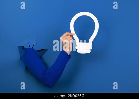 Hand halten Glühlampe über blauem Hintergrund Stockfoto