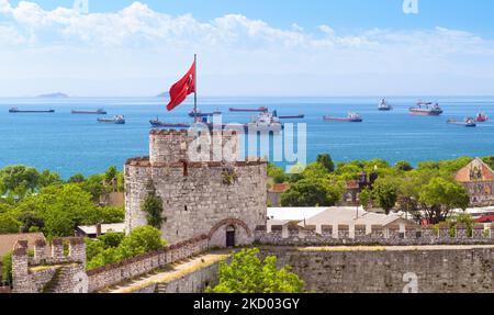 Yedikule Festung mit Blick auf das Meer von mit Schiffen, Istanbul, Türkei. Malerische Aussicht auf das alte Schloss, die türkische Flagge und Frachtschiffe. Thema des Getreideexports Stockfoto