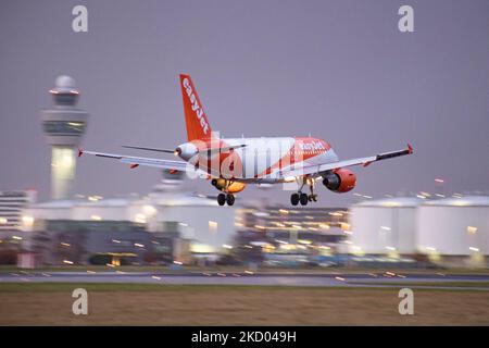 EasyJet Airbus A319-Flugzeuge, wie sie beim endgültigen Anflug und der Landung auf dem Flughafen Amsterdam Schiphol AMS EHAM mit dem Kontrollturm und dem Flughafenterminal im Hintergrund am Abend zu sehen sind. Das ankommende Flugzeug der britischen multinationalen Billigfluggesellschaft hat die Registrierung G-EZFU. Die Luft- und Passagierindustrie befindet sich in einer schwierigen Phase, da die Coronavirus-Pandemie Covid-19 negative Auswirkungen auf die Reisebranche hat, mit Befürchtungen über die Verschlechterung der Situation aufgrund der neuen Omega-Variantenmutation. Amsterdam, Niederlande am 5. Januar 2022 (Foto: Nicol Stockfoto