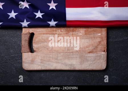 USA-Flagge in der Nähe von leerem Holzbrett auf dunklem Marmorhintergrund, Konzept der amerikanischen Küche, Layout-Bild Stockfoto