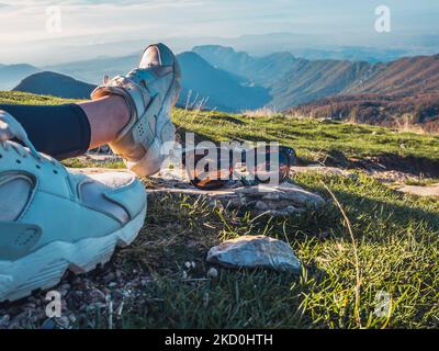 Die Beine der Frau liegen auf dem Berg. Ruhen Sie sich aus, nachdem Sie den Gipfel des Berges erreicht haben. Nahaufnahmen von Sonnenbrillen in den Bergen. Damensonnenbrille i Stockfoto