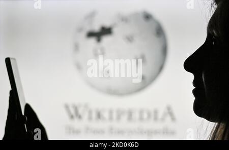 Ein Bild einer Frau, die ein Mobiltelefon vor das Wikipedia-Logo hält, das auf einem Computerbildschirm angezeigt wird. Am Dienstag, den 12. Januar 2021, Kanada. (Foto von Artur Widak/NurPhoto) Stockfoto