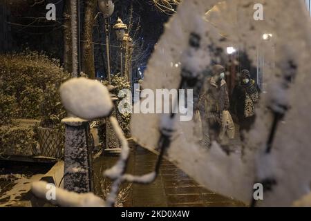 Zwei iranische Frauen, die Schutzmasken tragen, gehen während einer verschneiten Nacht im Norden Teherans am 20. Januar 2022 entlang einer Straße. (Foto von Morteza Nikoubazl/NurPhoto) Stockfoto