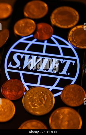 DAS SWIFT-Logo (Society for Worldwide Interbank Financial Telecommunication), das auf einem Telefonbildschirm angezeigt wird, und die Münzen sind auf diesem Bild zu sehen, das am 23. Januar 2022 in Krakau, Polen, aufgenommen wurde. (Foto von Jakub Porzycki/NurPhoto) Stockfoto
